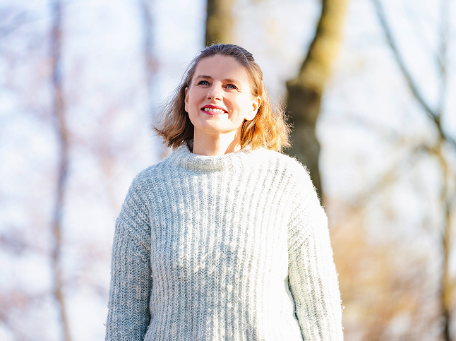 Alexandra steht im Wald und lächelt während sie leicht nach oben blickt.