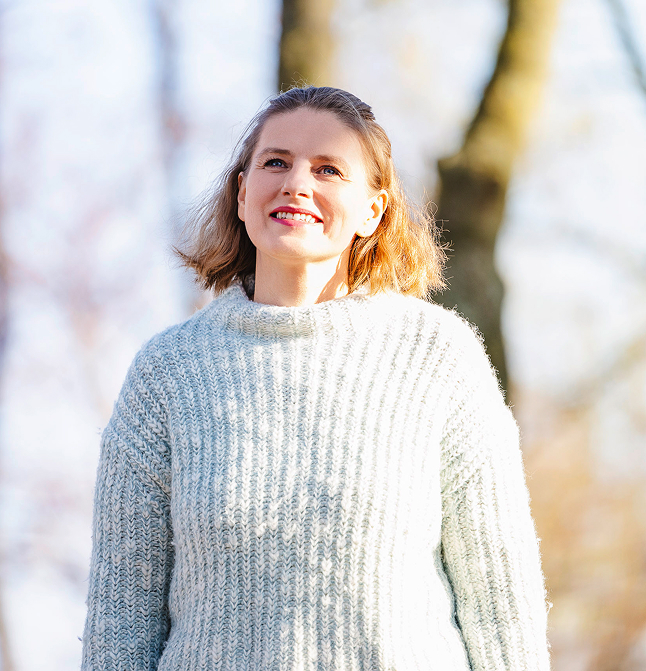 Alexandra steht im Wald und lächelt während sie leicht nach oben blickt.